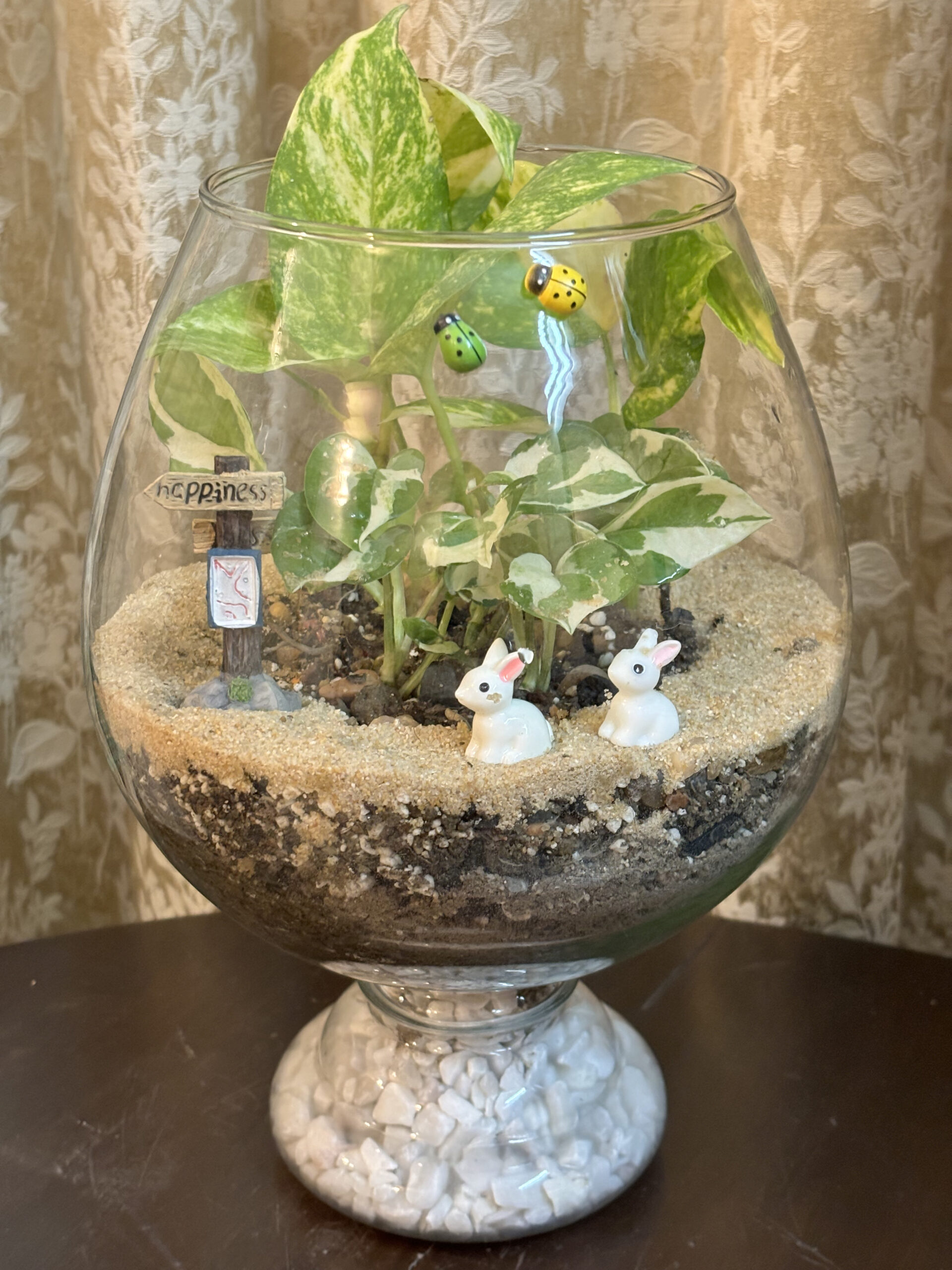 Mini garden terrarium with plants and tiny bunny figurines.